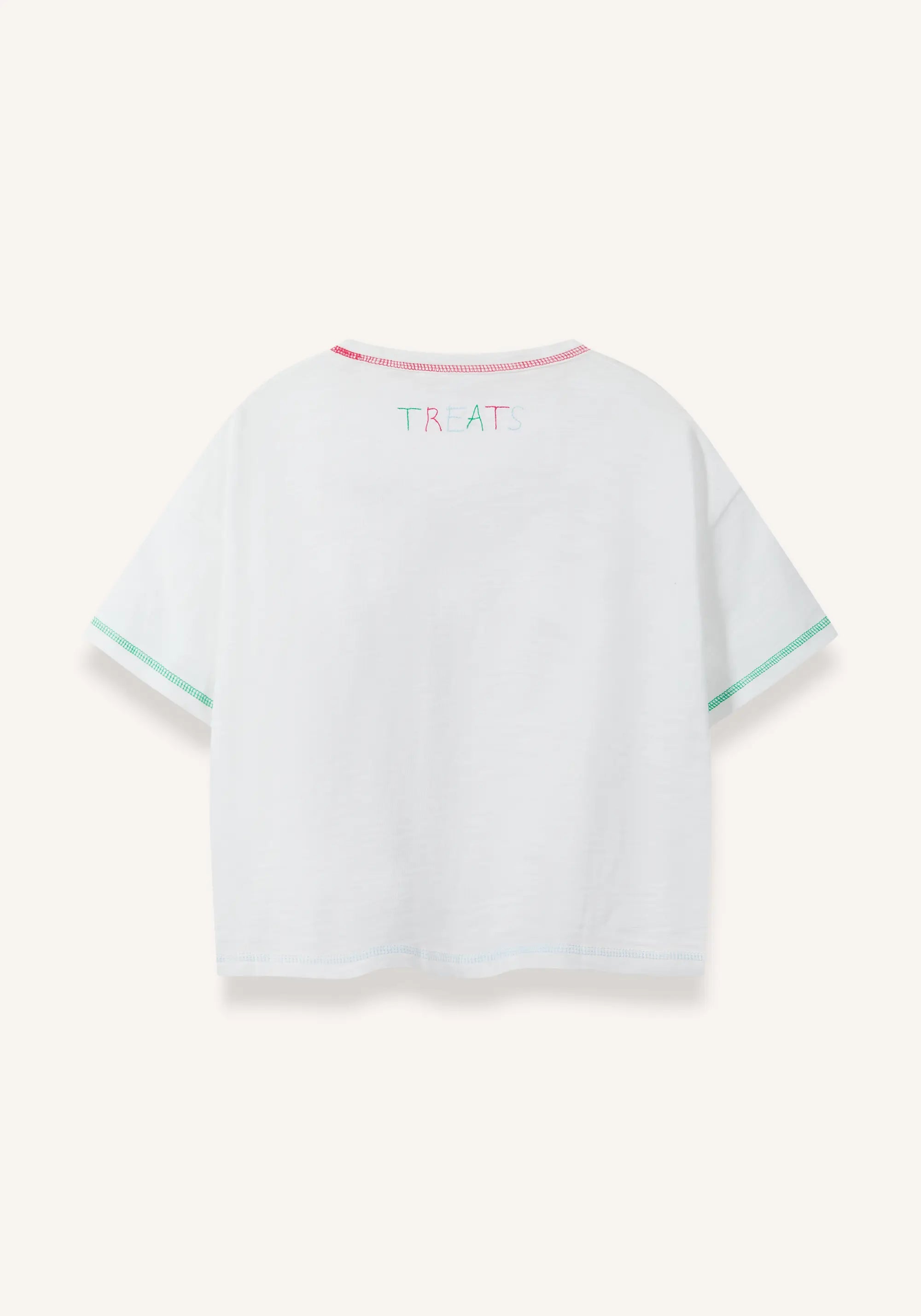 White short-sleeve T-shirt shown from the back, featuring a small multicolor 'TREATS' graphic on the upper back, pink trim along the collar, and mint green trim along the sleeve cuffs, set against a light cream background.